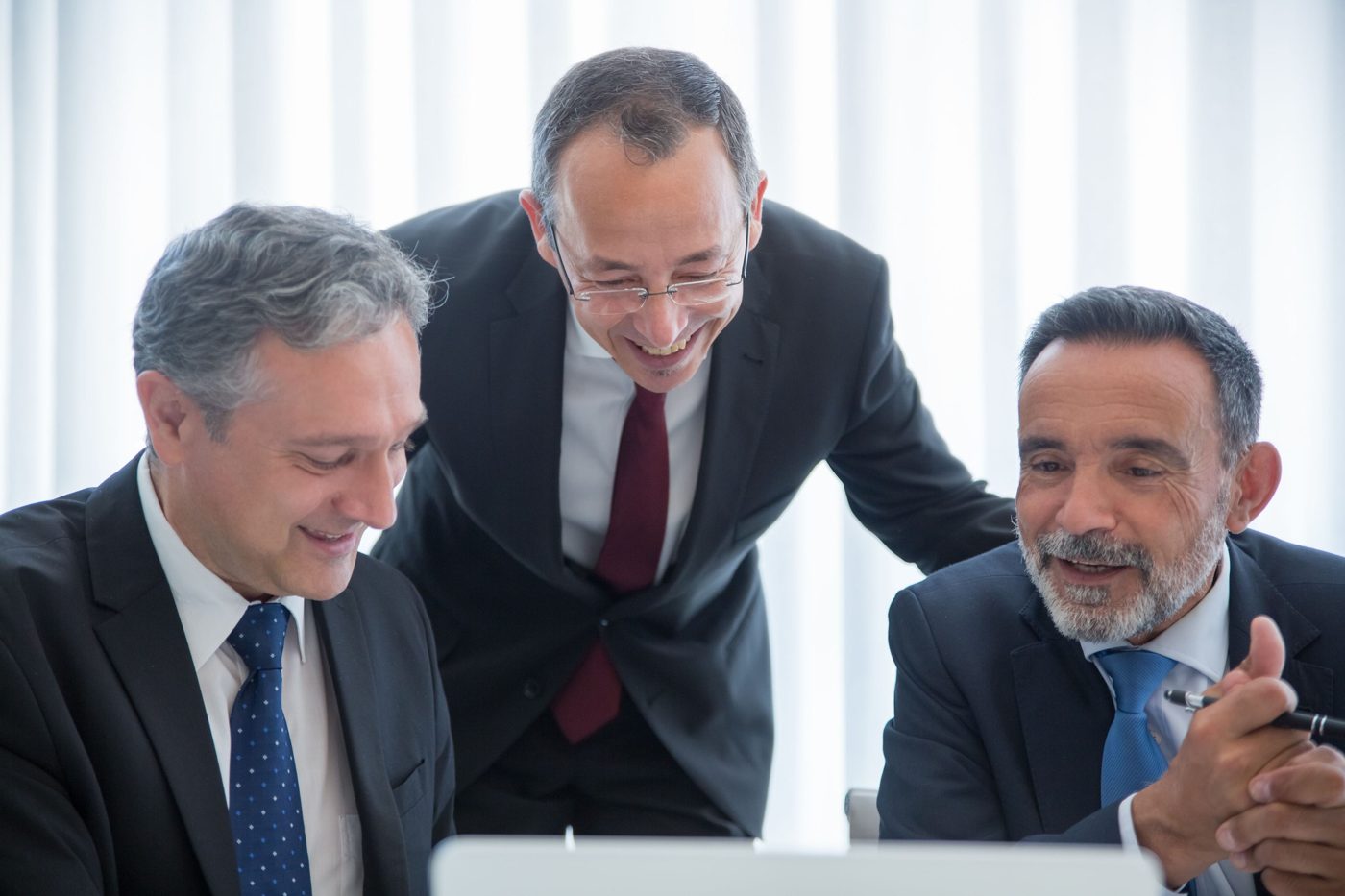 Three executives smiling while reviewing a laptop